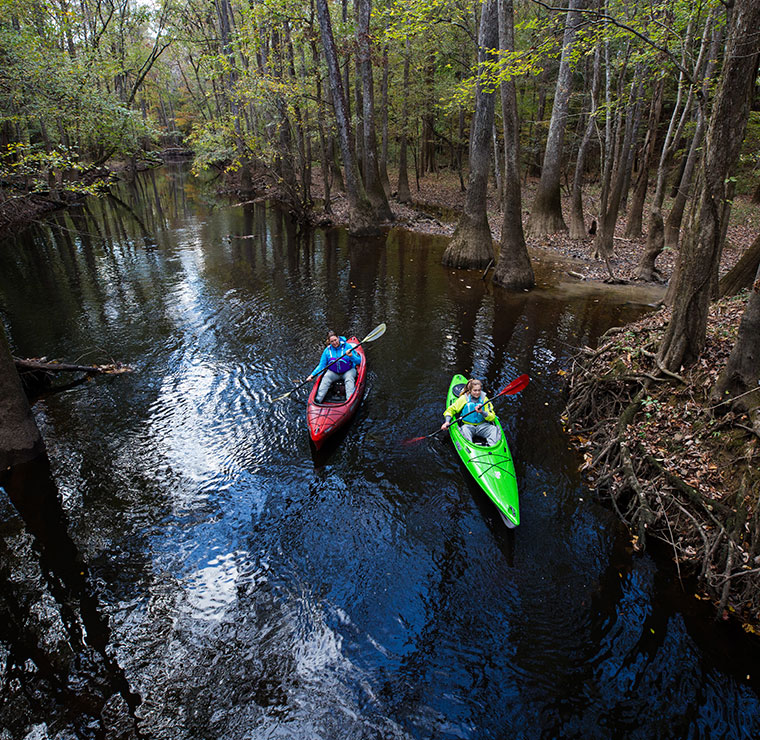 2 girls kayaking Jackson Kayaks in a creek in the woods.
